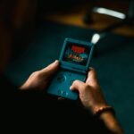 Close-up of individual holding a retro handheld gaming device, playing a classic video game indoors.